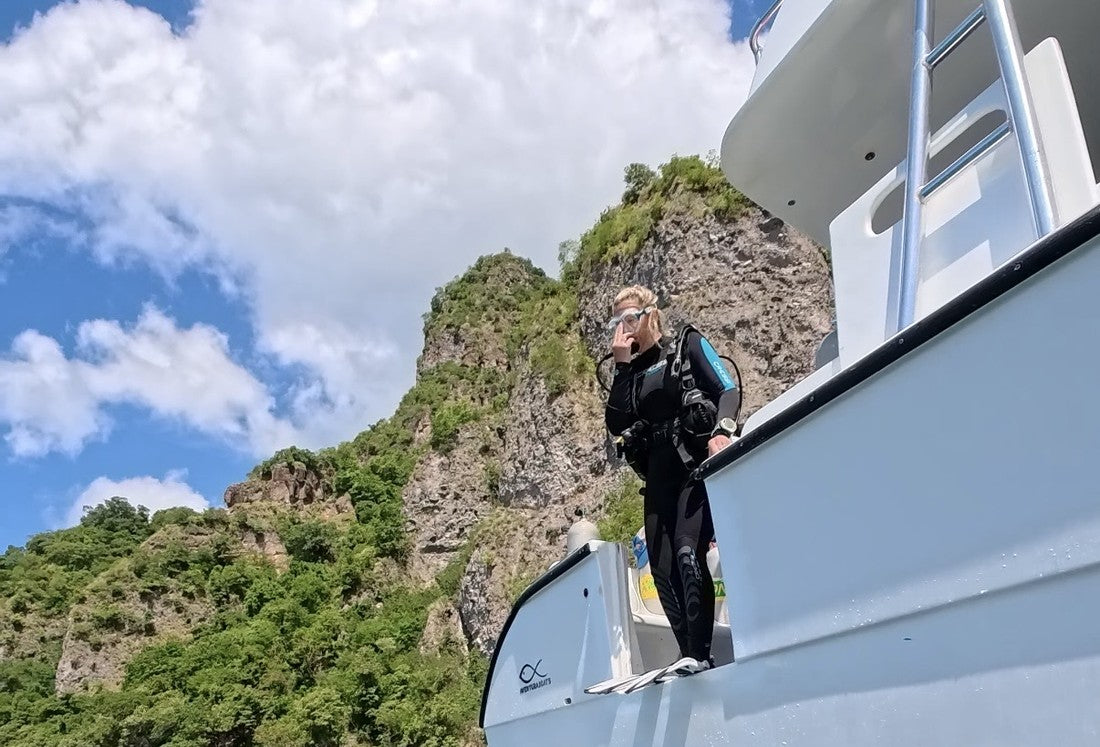 A Dive Arizona diver stepping off the boat's dive platform beneath island cliffs